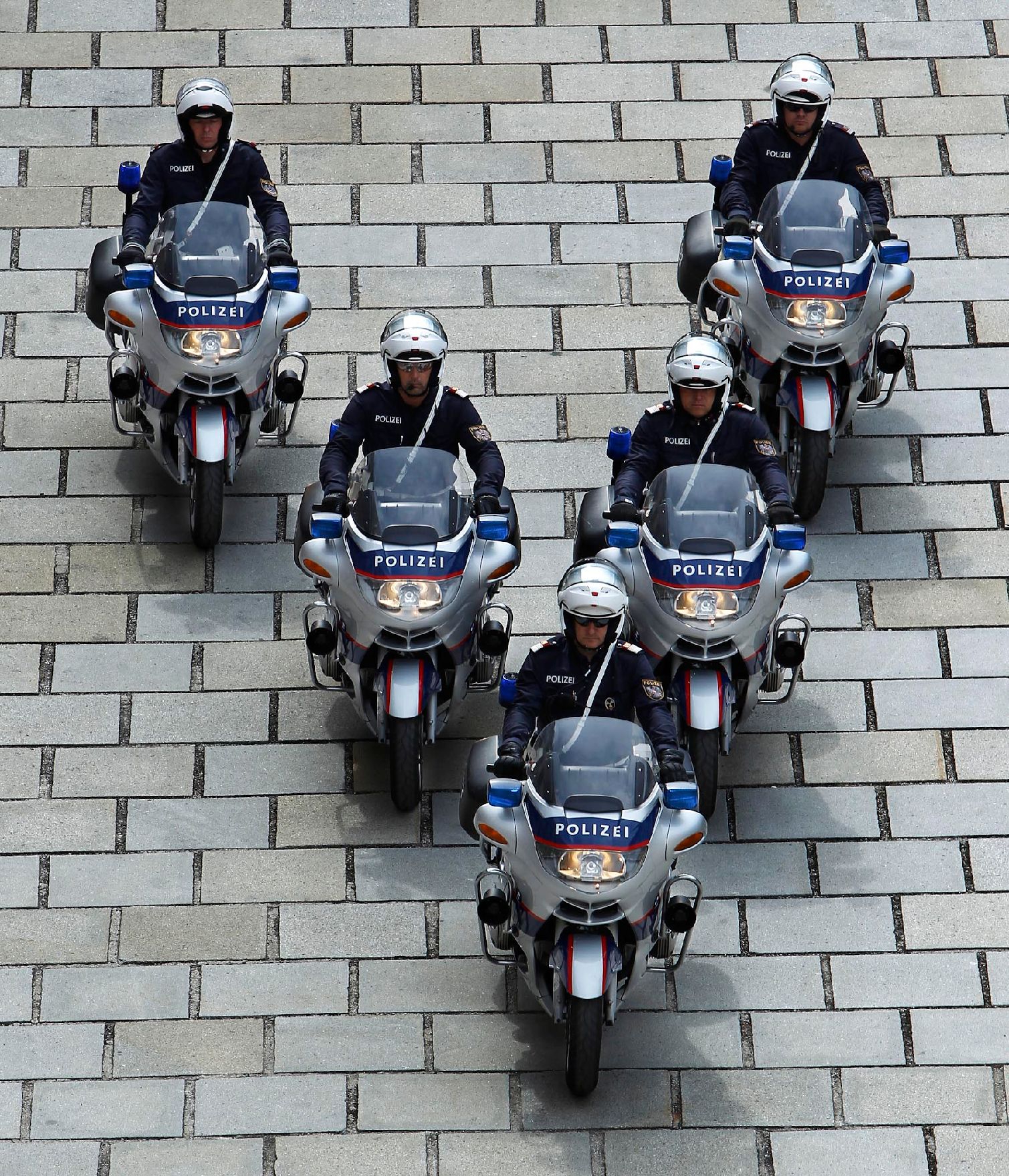 Polizisten mit Motorrädern in V-Formation. Schlagworte: Blaulicht, Eskorte, Fahrzeug, Mann, Mensch, Motorrad, Pflasterstein, Polizei, Sicherheit, Staatsbesuch, Sturzhelm, Uniform, Verkehr