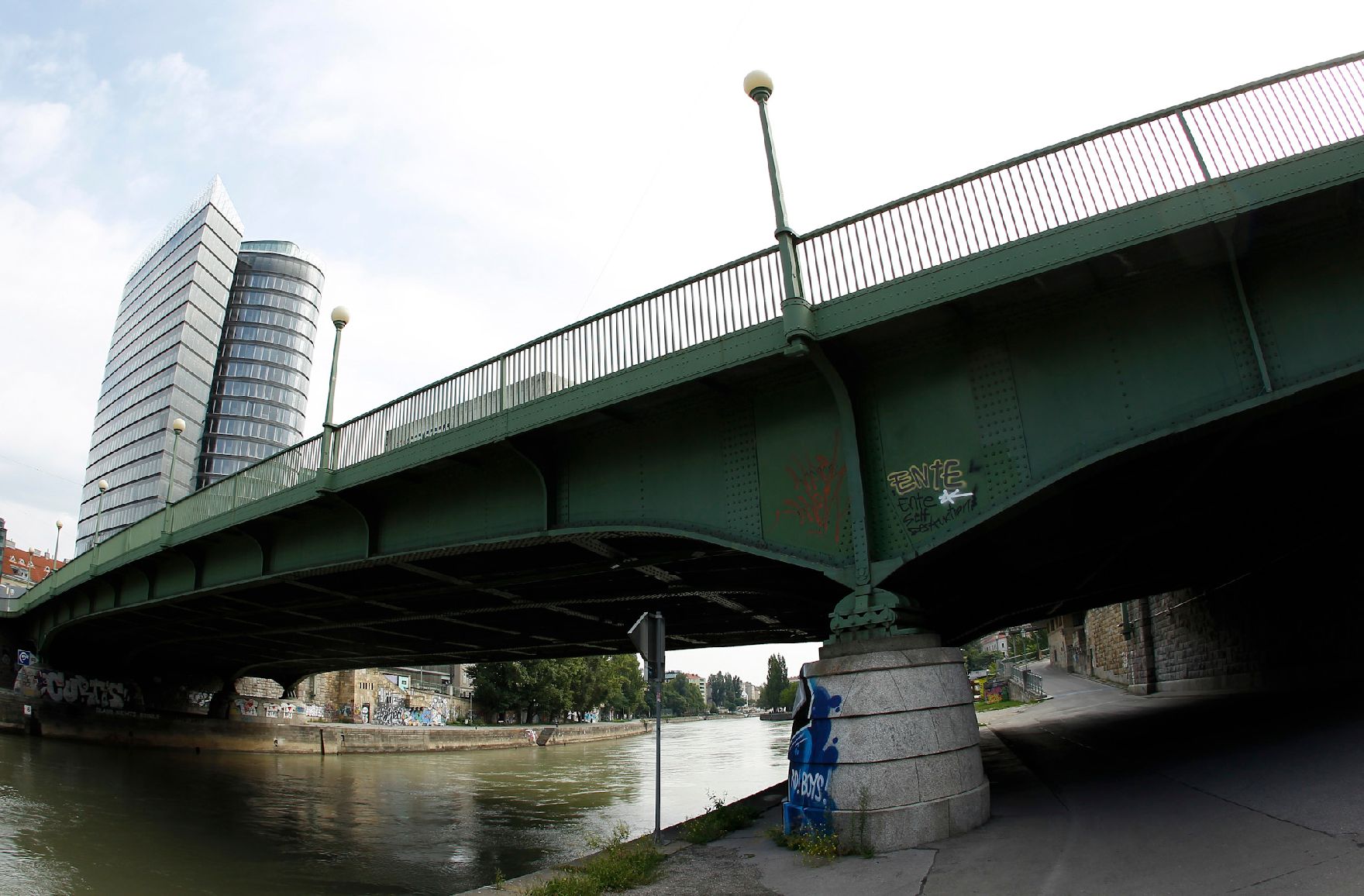 Brücke über den Donaukanal, mit einem Hochhaus im Hintergrund. Schlagworte: Fluß, Graffitis, Himmel, Laterne, Stadtlandschaft, Wasser, Wolken