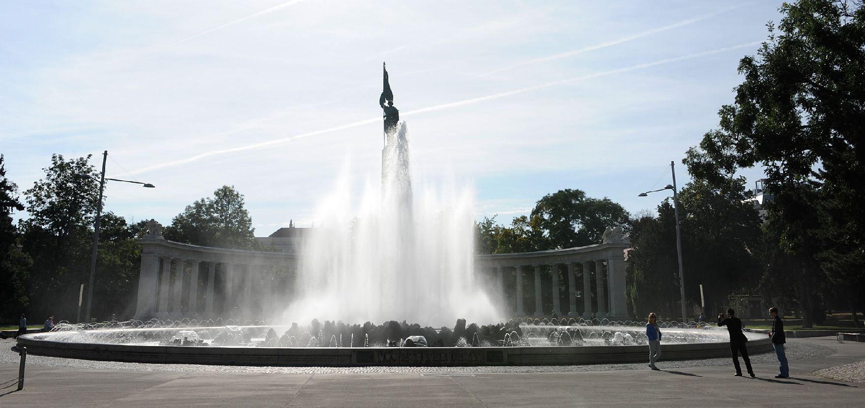 Der Hochstrahlbrunnen am Schwarzenbergplatz. Schlagworte: Brunnen, Himmel, Stadtlandschaft, Statue, Wasser, Wolken