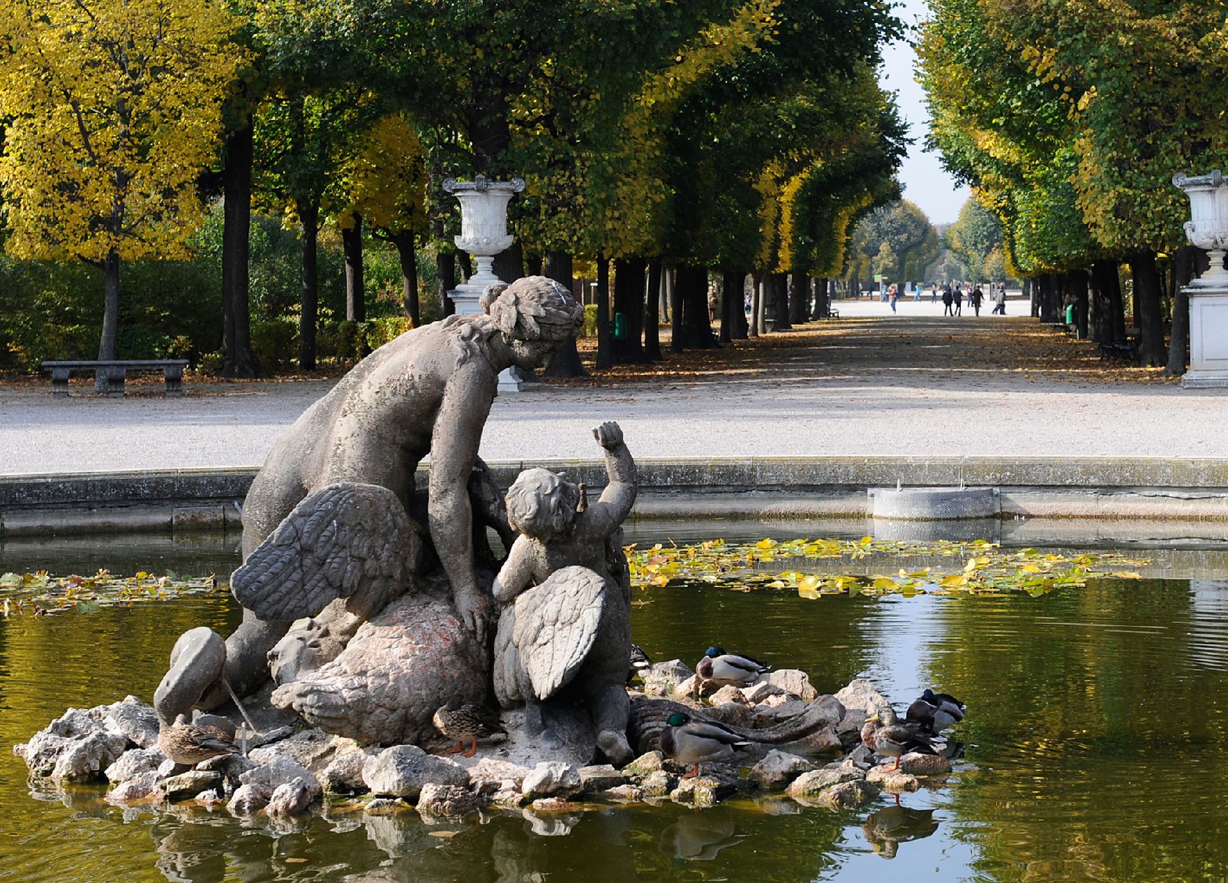 Statue in einem der Brunnen des Parks von Schloss Schönbrunn, im Hintergrund eine herbstliche Allee. Schlagworte: Brunnen, Schönbrunn, Stadtlandschaft, Wasser