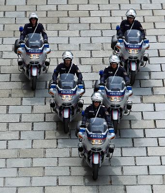 Polizisten mit Motorrädern in V-Formation. Schlagworte: Blaulicht, Eskorte, Fahrzeug, Mann, Mensch, Motorrad, Pflasterstein, Polizei, Sicherheit, Staatsbesuch, Sturzhelm, Uniform, Verkehr