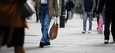 Eine Person mit Einkaufstasche. Schlagworte: Beine, Einkaufstasche, Füße, Hose, gehen, Menschen, Schuhe, Wirtschaft
