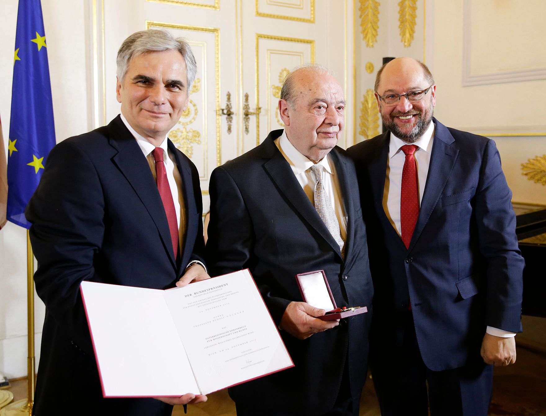 Am 4. Dezember 2015 &uuml;berreichte Bundeskanzler Werner Faymann (l.) das &ouml;sterreichische Ehrenkreuz f&uuml;r Wissenschaft und Kunst an Rudolf Gelbard (m.). Im Bild mit dem EU-Parlamentspr&auml;sidenten Martin Schulz (r.).