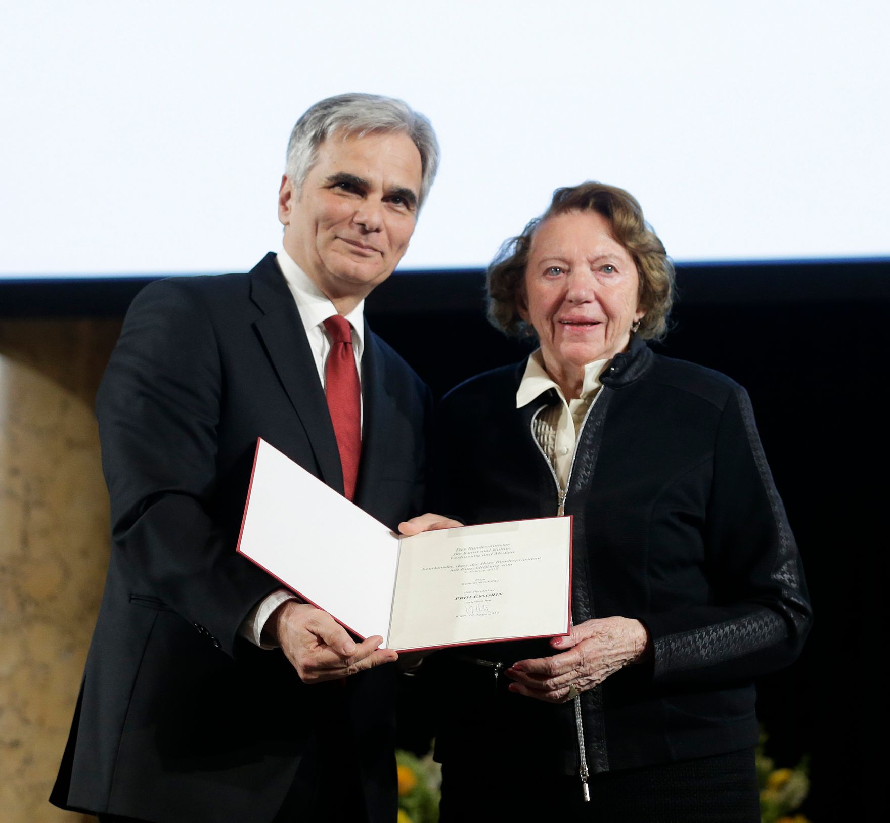 Am 8. April 2016 &uuml;berreichte Bundeskanzler Werner Faymann (l.) die Urkunde, mit der Katharina Sasso (r.) der Berufstitel Professorin verliehen wurde.