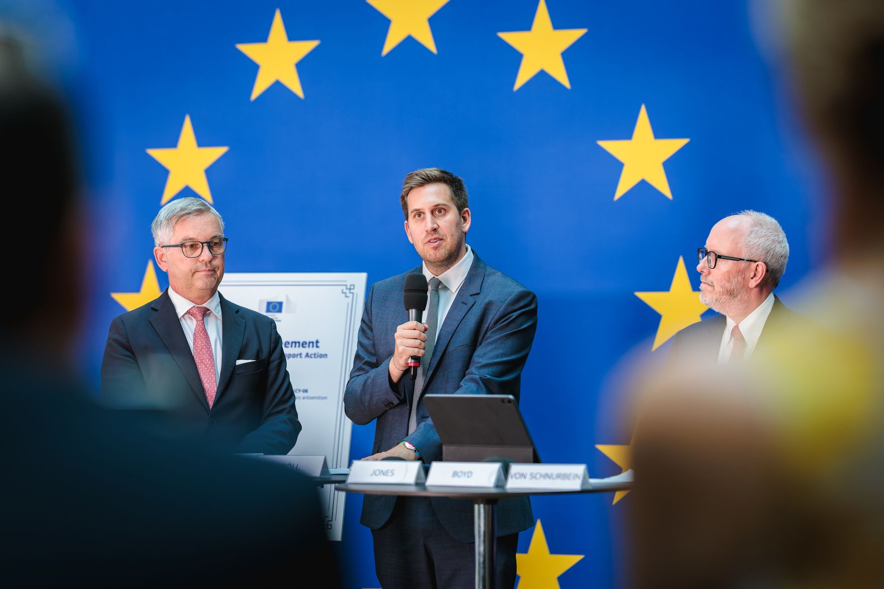 Am 29.06.2026 gab Staatssekret&auml;r Alexander Pr&ouml;ll (m.) gemeinsam mit EU-Kommissar Magnus Brunner (l.), Jonathan Boyd und Erik Jones (r.) eine Pressekonferenz zum Thema EU-Forschungsnetzwerk NERON (Network for European Research on Jewish Life and Antisemitism).