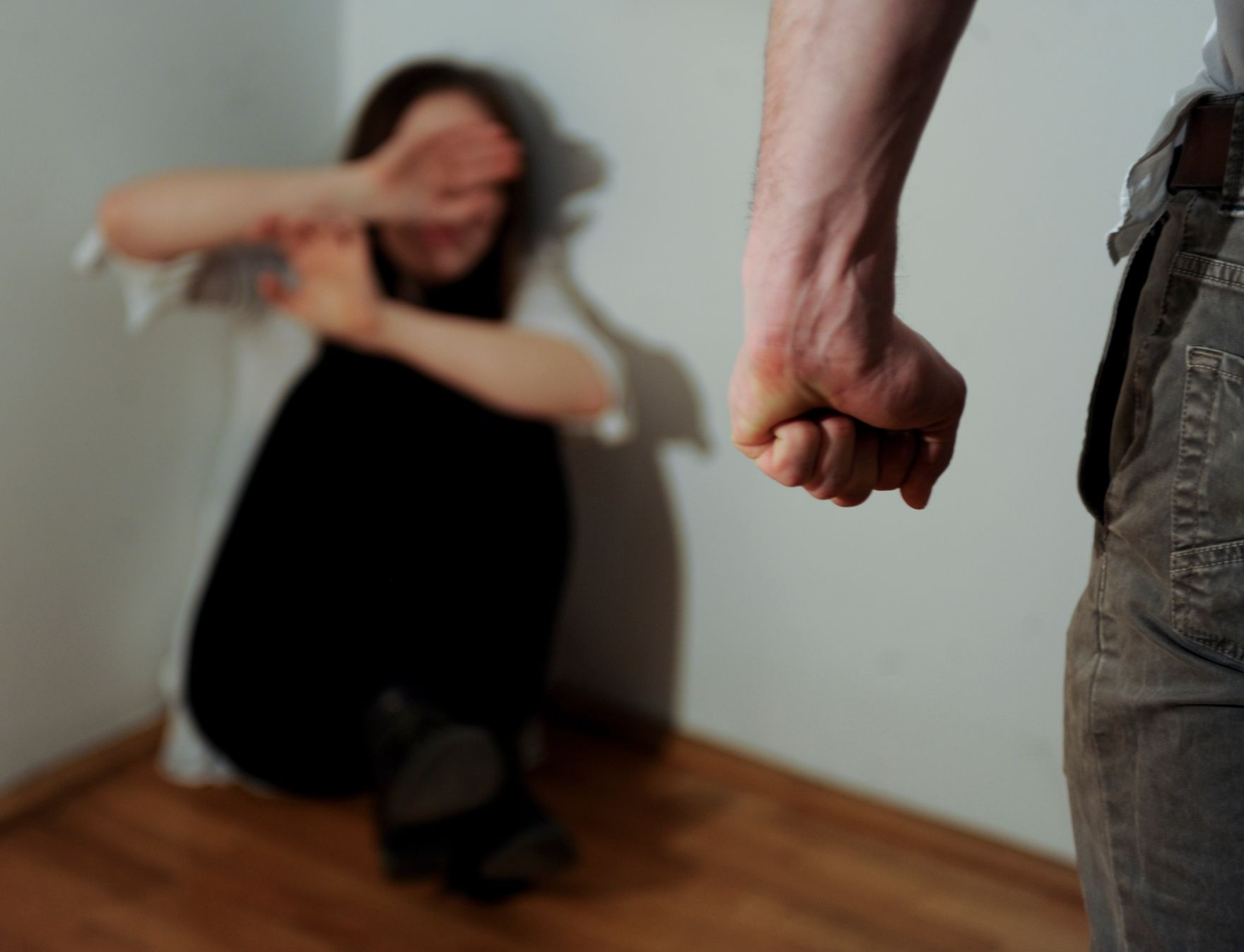 Eine &auml;ngstliche Frau kauert in einer Zimmerecke. Mann mit geballter Faust. Schlagworte: Abwehr, Angst, Faust, Frau, Gewalt, Mann, Menschen, schlagen