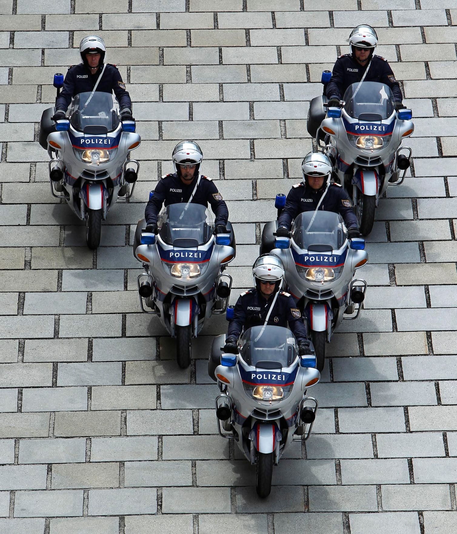 Polizisten mit Motorr&auml;dern in V-Formation. Schlagworte: Blaulicht, Eskorte, Fahrzeug, Mann, Mensch, Motorrad, Pflasterstein, Polizei, Sicherheit, Staatsbesuch, Sturzhelm, Uniform, Verkehr