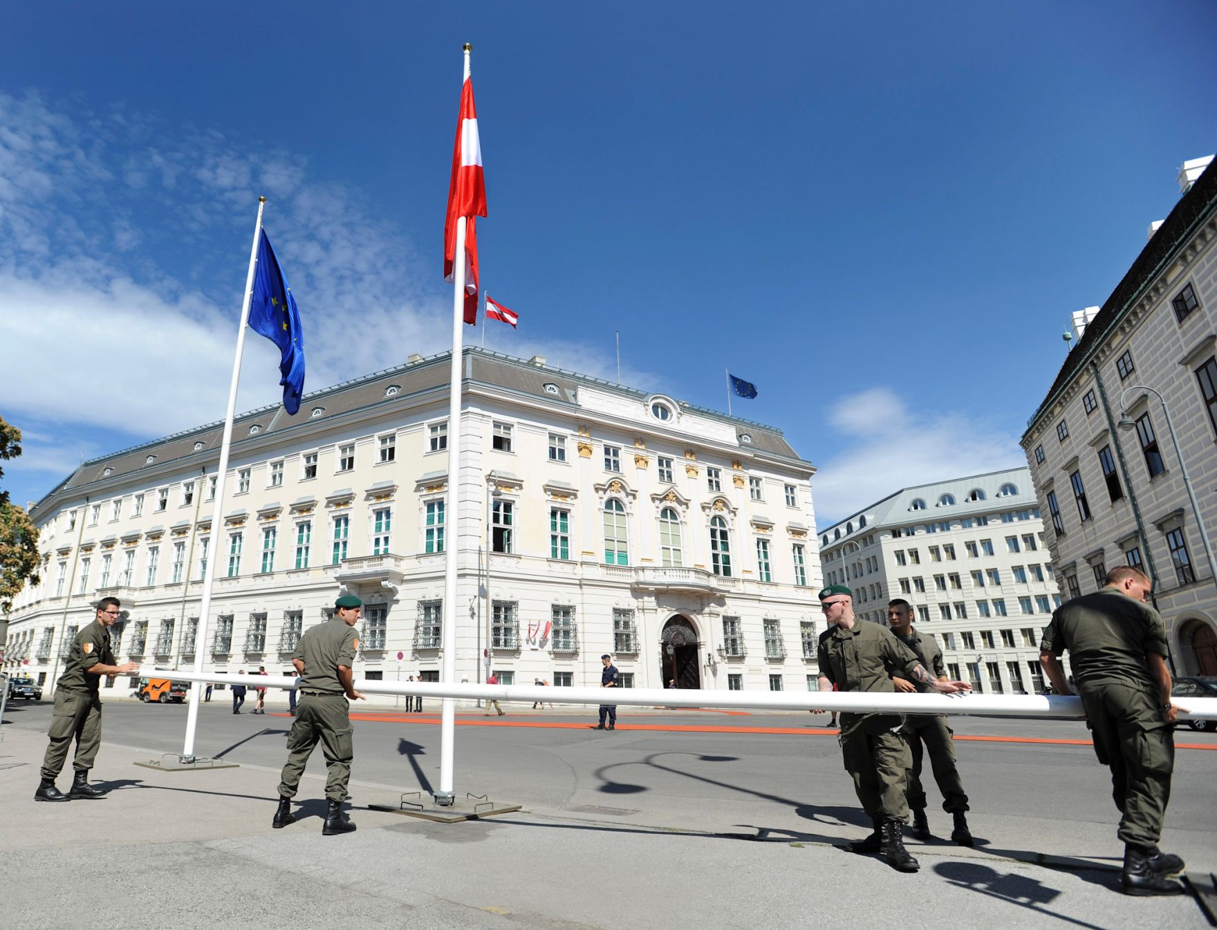 Soldaten beim Aufstellen von Fahnenmasten am Ballhausplatz. Im Bild ein roter Teppich, die &ouml;sterreichische und die europ&auml;ische Fahne. Schlagworte: Bundesheer, Bundeskanzleramt, Europa, Flaggen, Mann, M&auml;nner, Mast, Menschen, Staatsbesuch, Stadtlandschaft