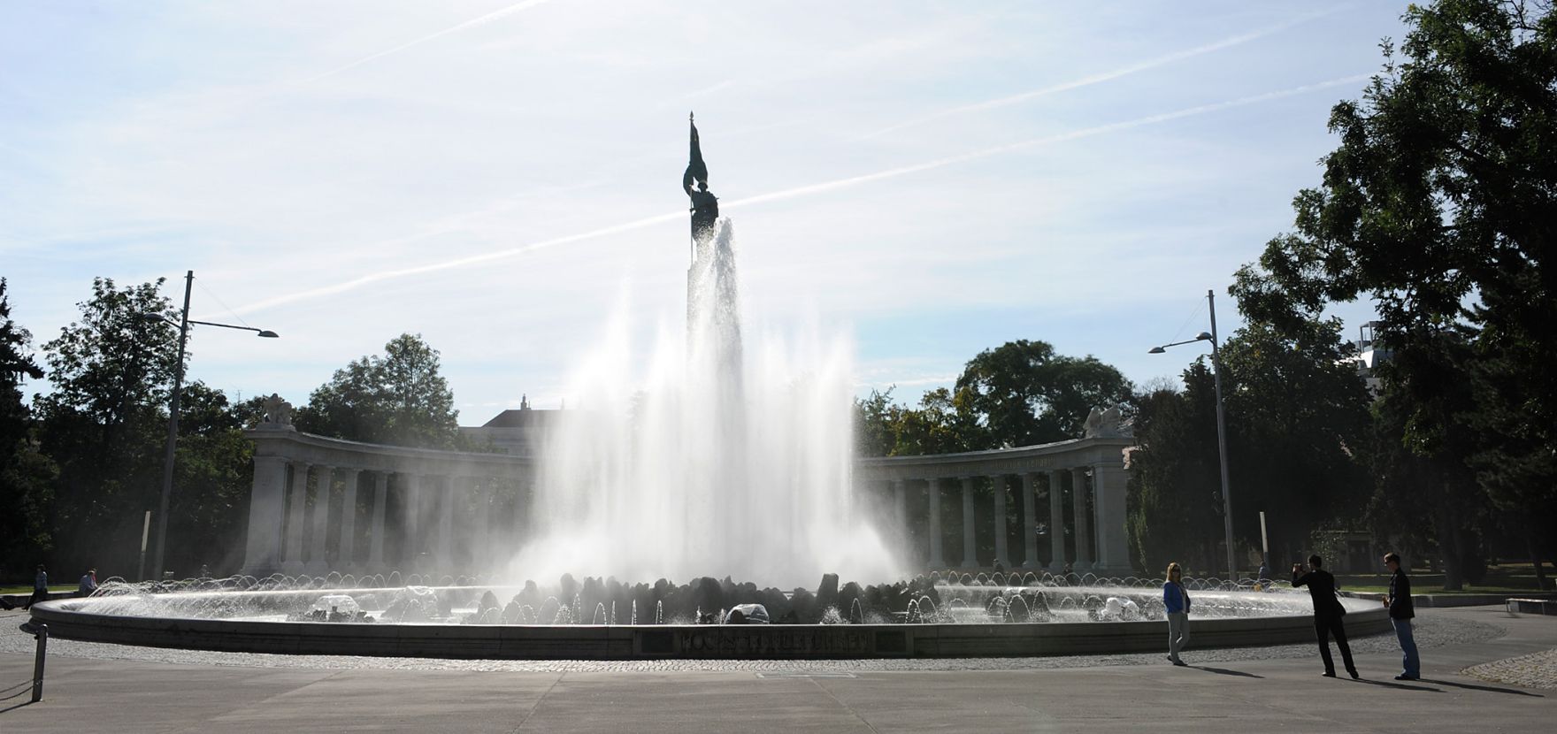 Der Hochstrahlbrunnen am Schwarzenbergplatz. Schlagworte: Brunnen, Himmel, Stadtlandschaft, Statue, Wasser, Wolken