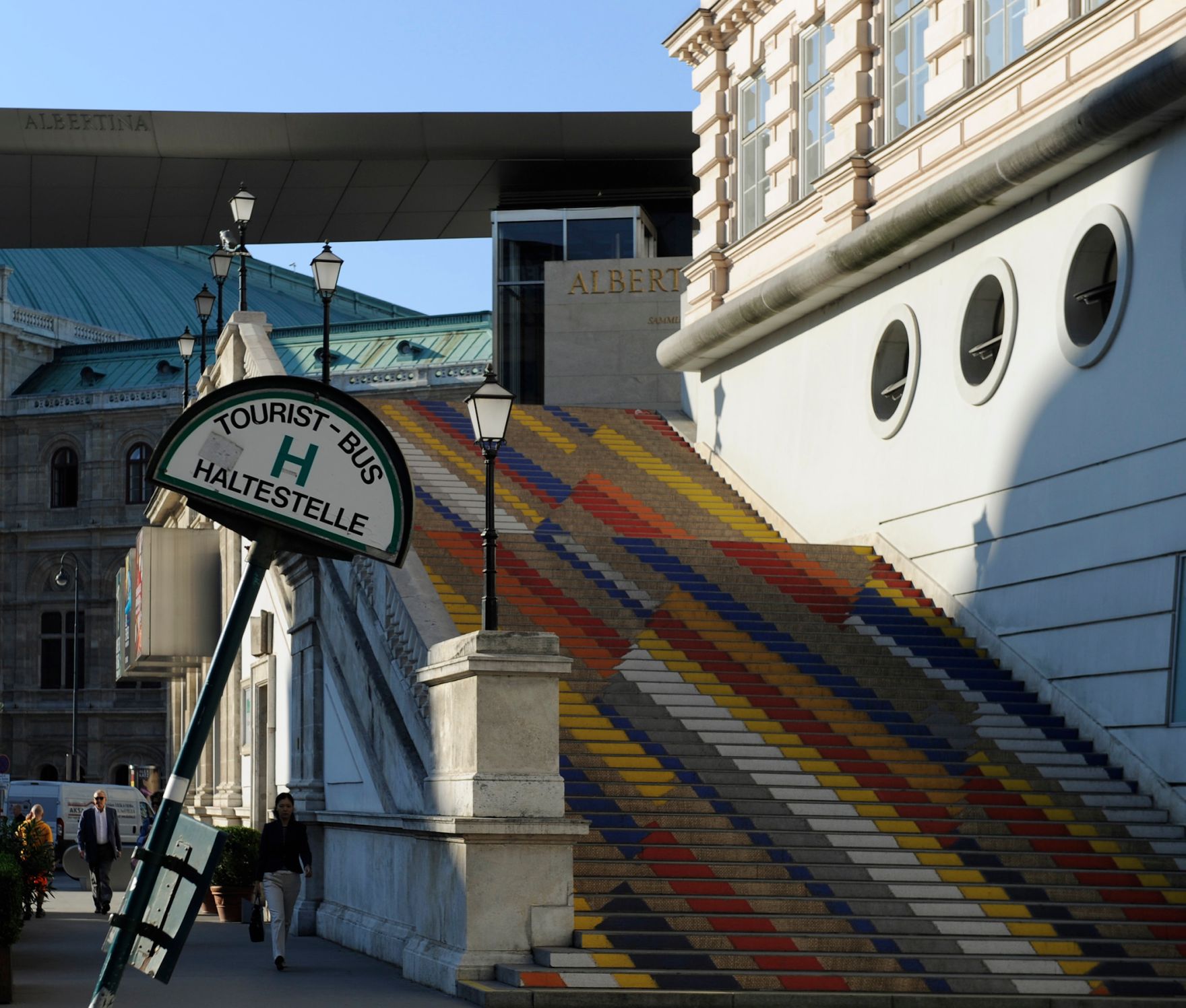 Ein schiefes Touristen-Bus Haltestellenzeichen vor dem bunten Stiegenaufgang der Albertina. Schlagworte: Ger&uuml;st, Laternen, Stadtlandschaft, Statuen, Stufen, Treppen