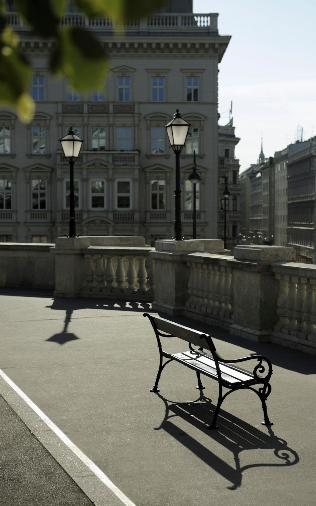 Eine Parkbank und Laternen auf dem Platz vor dem Eingang der Albertina. Schlagworte: Bank, Geb&auml;ude, Holz, Parkbank, Stadtlandschaft