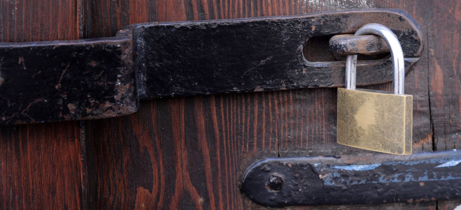 Eine &Uuml;berwurffalle mit Vorh&auml;ngeschloss. Schlagworte: Beschlag, B&uuml;gel, Metall, Stadtlandschaft, Statuen, Tor, T&uuml;r