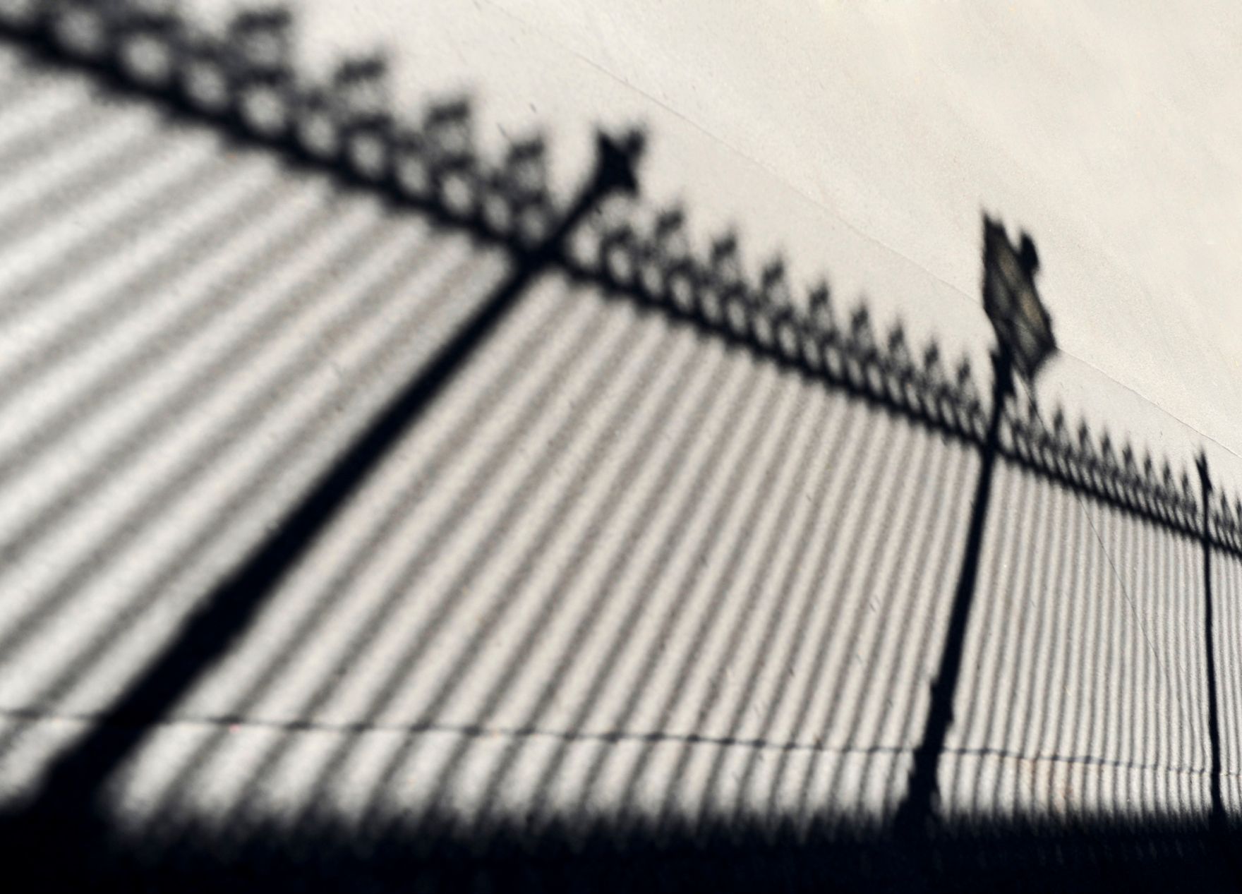 Der Schatten einer Zauns mit Laterne. Schlagworte: Gitter, Laterne, Schatten, Stadtlandschaft, Zaun