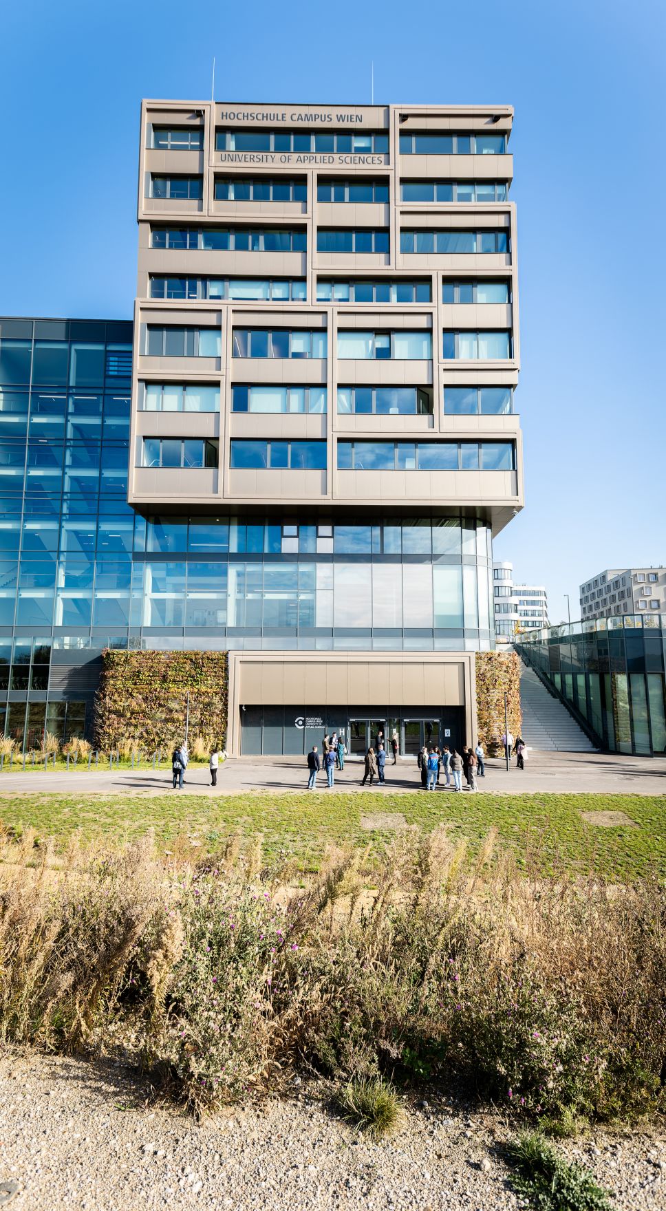 Hochschule Campus Wien au&szlig;en &ndash; Moderner Hochschulkomplex mit Glasfassade und weitl&auml;ufigem Vorplatz Hochschule Campus Wien, Fachhochschule Wien, Hochschule, Studium, Bildung, Forschung, Wissenschaft, Universit&auml;tsgeb&auml;ude, moderner Campus, Architektur, Glasfassade, Neubau, Bildungseinrichtung, Favoriten, 10. Bezirk Wien, Stadtentwicklung, Lifesciences, Technik, Gesundheitswesen, Soziales, modernes Wien, urbaner Raum, nachhaltige Architektur, Bildungscampus