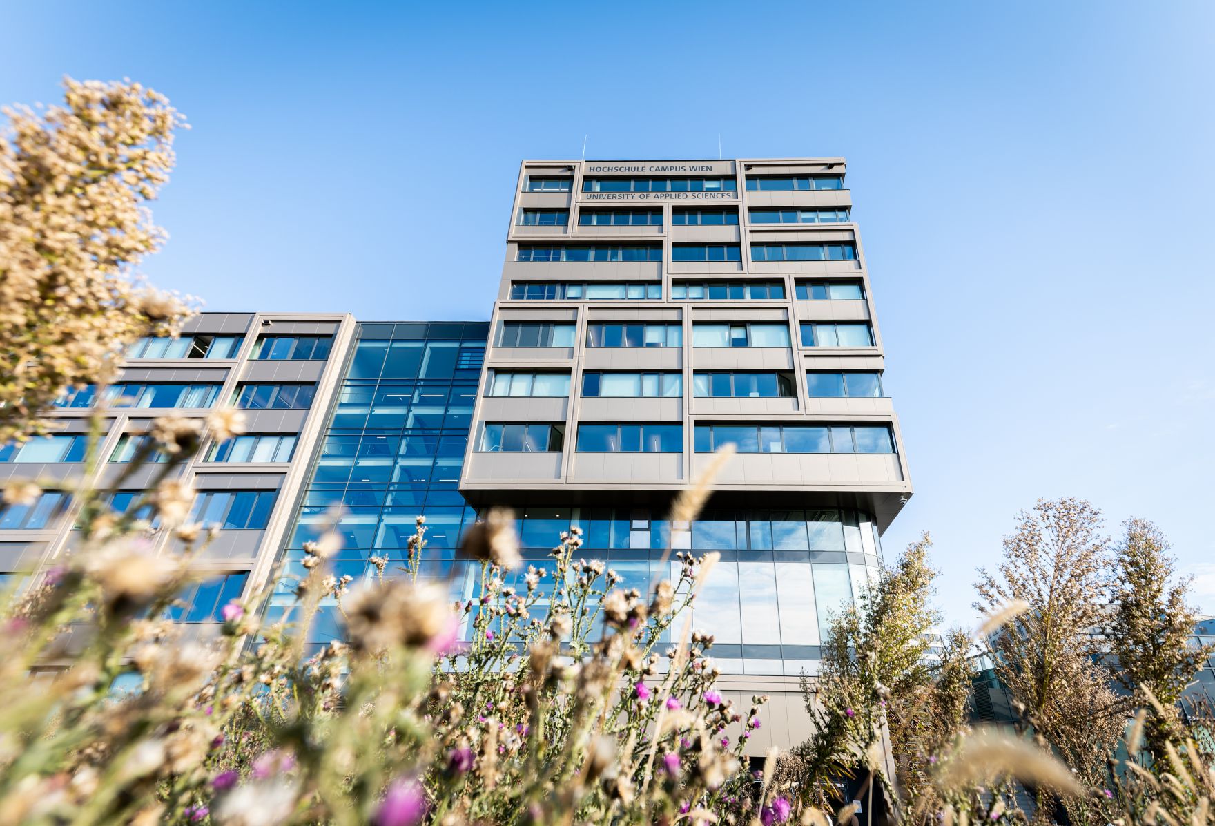 Hochschule Campus Wien au&szlig;en &ndash; Moderner Hochschulkomplex mit Glasfassade und weitl&auml;ufigem Vorplatz Hochschule Campus Wien, Fachhochschule Wien, Hochschule, Studium, Bildung, Forschung, Wissenschaft, Universit&auml;tsgeb&auml;ude, moderner Campus, Architektur, Glasfassade, Neubau, Bildungseinrichtung, Favoriten, 10. Bezirk Wien, Stadtentwicklung, Lifesciences, Technik, Gesundheitswesen, Soziales, modernes Wien, urbaner Raum, nachhaltige Architektur, Bildungscampus
