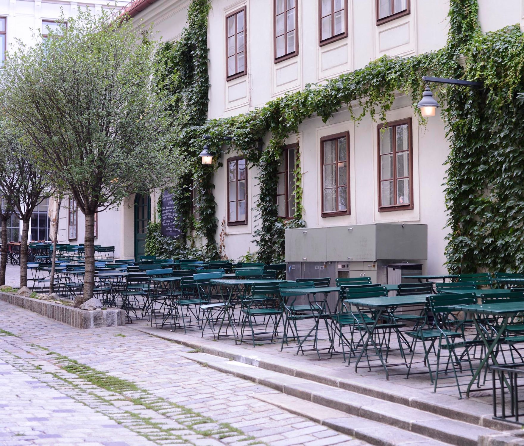Ein Gastgarten am Spittelberg. Schlagworte: B&auml;ume, Fenster, Gastronomie, Geb&auml;ude, Laternen, Lokal, Stadtlandschaft, Sessel, St&uuml;hle, Tische, Wirtschaft