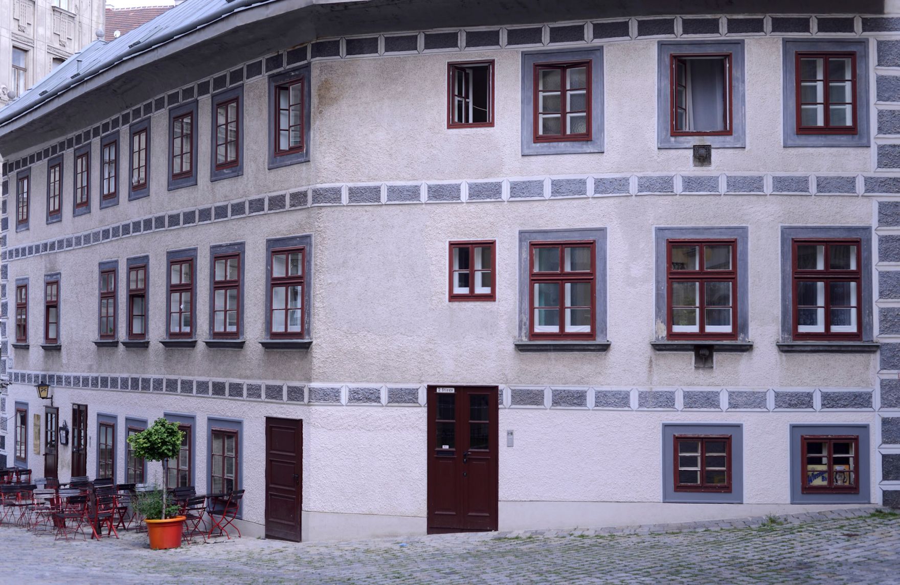 Wohnhaus und Gastgarten im Ersten Bezirk. Schlagworte: Fenster, Gastronomie, Geb&auml;ude, Lokal, Stadtlandschaft, Sessel, St&uuml;hle, Tische, Wirtschaft