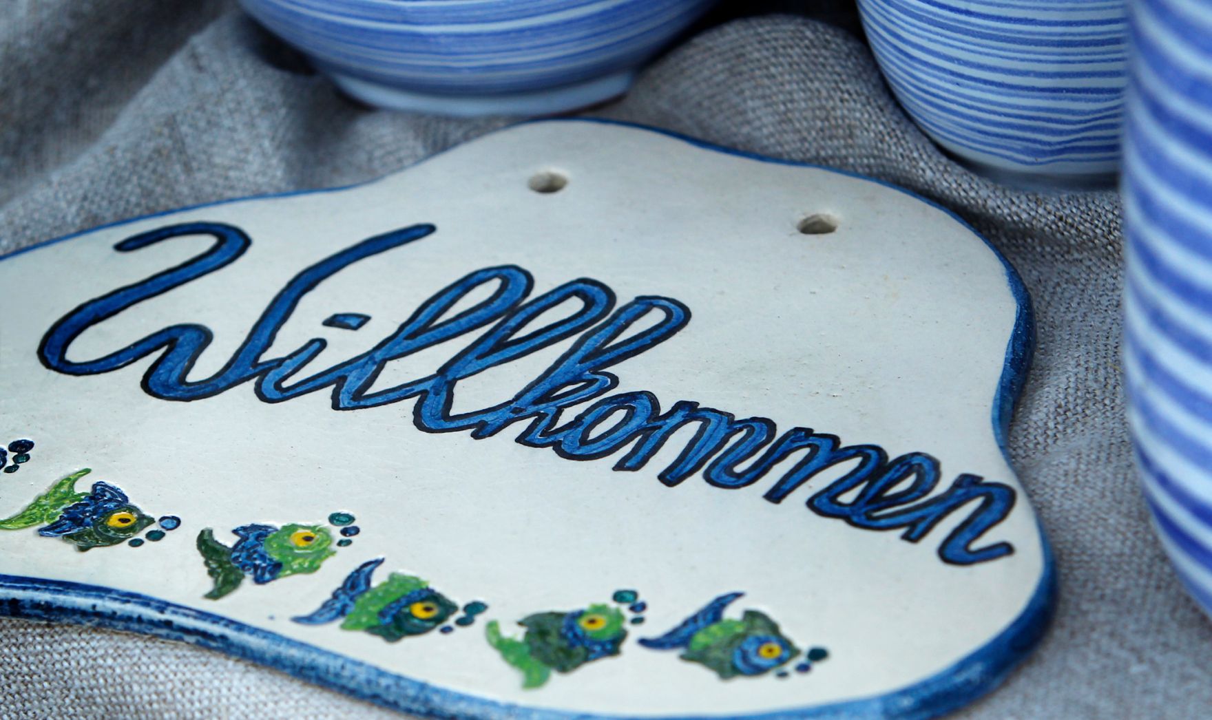 Ein bemaltes Keramikschild mit der Aufschrift "Willkommen". Schlagworte: Bauernmarkt, Beschriftung, Fische, Handwerk, Markt, Marktst&auml;nde, Schild, Wirtschaft