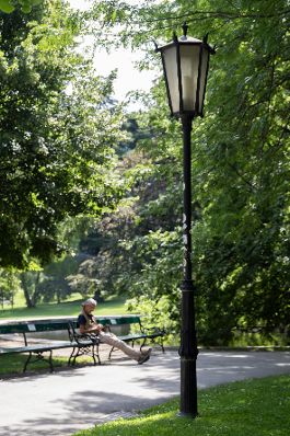 Person sitzt auf einer Parkbank im Burggarten. Schlagw&ouml;rter: Parkbank, Innenstadt, Baum, Lampe