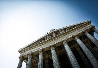 Die S&auml;ulen am Haupteingang des Parlamentsgeb&auml;udes. Ein Vogel fliegt vor dem Dach vorbei. Schlagworte: Architektur, Brunnen, Denkmal, Geb&auml;ude, Statue, Sehensw&uuml;rdigkeit, Stadtlandschaft, Tier, Vogel