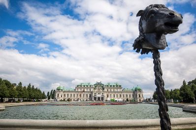 Pferdestatue des chinesischen K&uuml;nstlers Ai Weiwei, mit dem Schloss Belvedere im Hintergrund und Installation der Schwimmwesten von Fl&uuml;chtlingen im Wasser. Schlagworte: Ai Weiwei, Architektur, Ausstellung, Belvedere, F Lotus, Geb&auml;ude, Himmel, Kunst, K&uuml;nstler, Pferd, Sehensw&uuml;rdigkeit, Schloss, Schwimmwesten, Statue, Teich Tierkreiszeichen, Wasser, Wolken