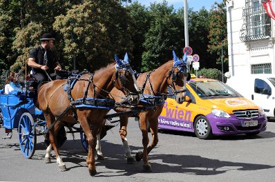 Ein blauer Fiaker f&auml;hrt am Ballhausplatz an einem orange-lila Taxi vorbei. Schlagworte: Auto, Fahrzeuge, Fiaker, Kutsche, Person, Pferde, PKW, Platz, Stadtlandschaften, Stra&szlig;e, Taxi, Tiere, Verkehr