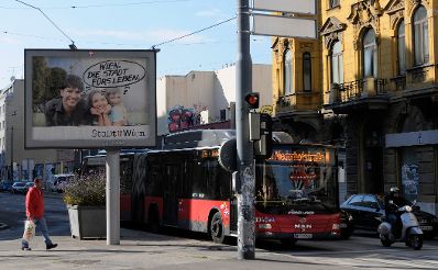 Eine Stra&szlig;enszene mit verschiedenen Verkehrsteilnehmern. Schlagworte: Autobus, Fahrzeuge, Fu&szlig;g&auml;nger, Moped, Motorrad, Person, Plakat, Stadtlandschaften, Stra&szlig;e, Verkehr, Werbung, Wiener Linien