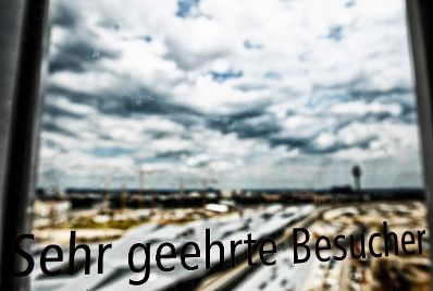 Die Baustelle des &Ouml;BB Hauptbahnhofes in Wien. Gesehen durch ein Fenster mit der Aufschrift &quot;Sehr geehrter Besucher&quot;. Schlagworte: Baustelle, Glas, Himmel, Wirtschaft, Wolken