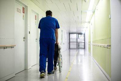 Gang - ein Krankenpfleger schiebt einen Patienten im Rollstuhl. Schlagwörter: Medizin, Gang, Rollstuhl, Patient, Krankenpfleger, Gesundheit, Behandlung, Rat für Beschäftigung, Sozialpolitik, Gesundheit und Verbraucherschutz, EPSCO