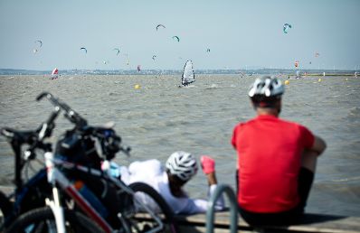 Radfahrer beobachten Kitesurfer am Neusiedlersee. Schlagwörter: Wind, See, Sport, Neusiedlersee, Wasser, Radfahrer, Rat für Bildung, Jugend, Kultur, Sport, EYC