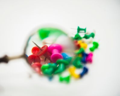 Verschiedenfärbige Pins unter einer Lupe Schlagworte: bunt, Büromaterial, Farben, Reißnägel