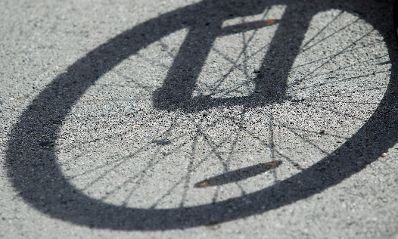 Der Schatten einer Fahrradreifens auf Asphalt. Schlagworte: Fahrrad, Fahrzeug, Reifen, Schatten, Speichen, Verkehr